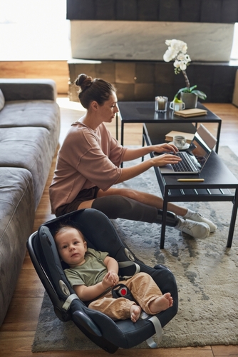 mother on computer with baby next to her in car seat